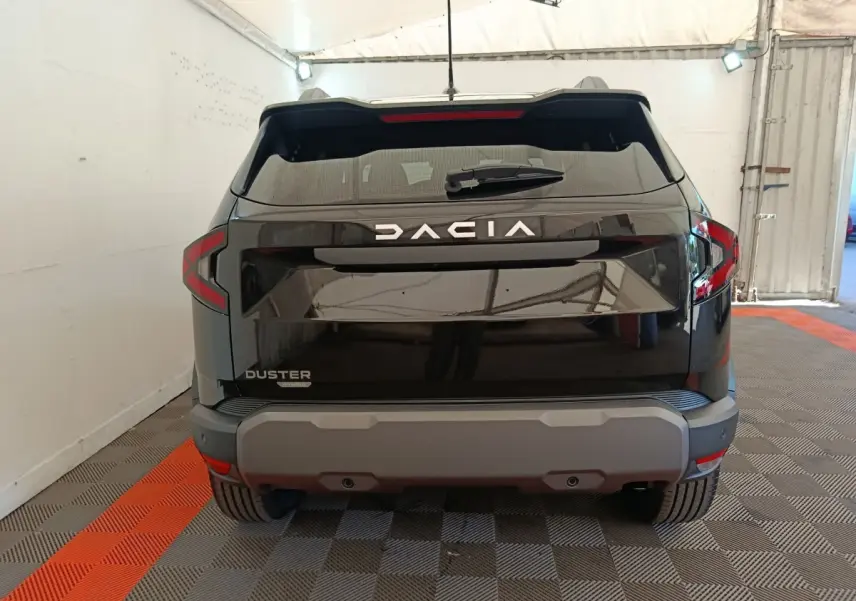 Vue arrière du Dacia Duster noir 2026 avec logo DACIA lumineux et pare-chocs gris dans un garage.