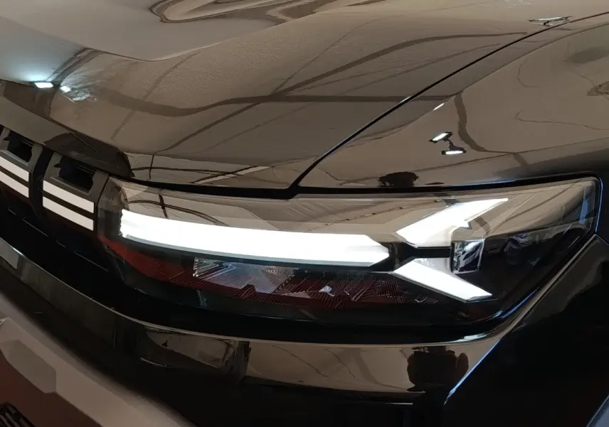 Gros plan sur le phare avant droit allumé du Dacia Duster Journey Hybrid 155 noir, soulignant ses lignes LED distinctives.