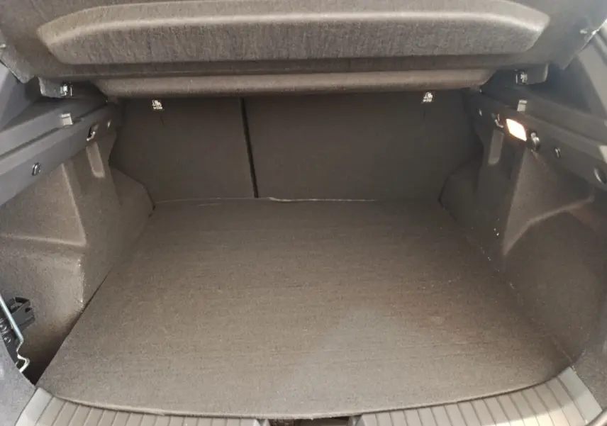 Vue intérieure du coffre noir du Dacia Duster Journey Hybrid 155, montrant l'espace de chargement avec tapis et éclairage latéral.
