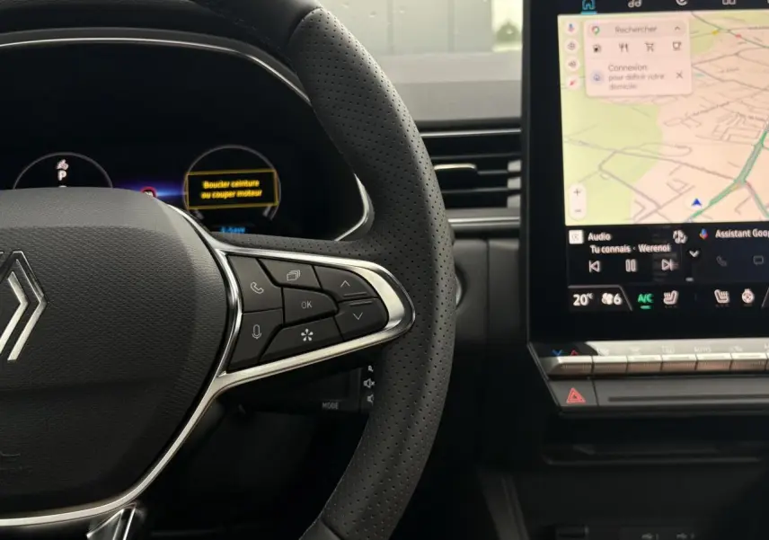 Gros plan sur le volant perforé et la console centrale avec écran tactile affichant la navigation du Renault Captur blanc nacré.