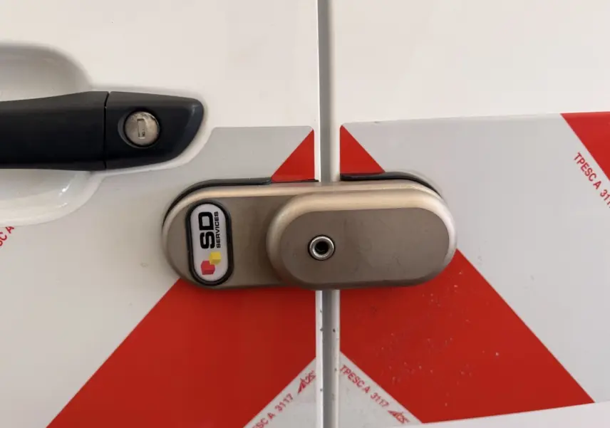 Gros plan sur la serrure arrière gauche d’un Citroën Berlingo blanc 2019 avec marquages rouges et dispositif de sécurité SD Services.