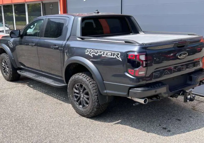 Ford Ranger Raptor 2025 gris météore vu en 3/4 arrière droit avec logo Raptor et pneus tout-terrain marqués.