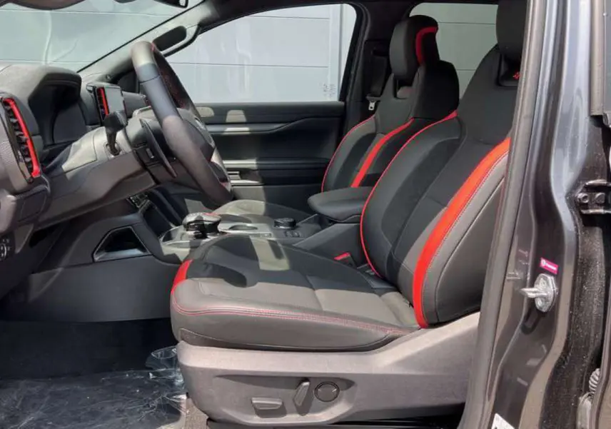 Intérieur du Ford Ranger Raptor 2025 en gris météore, vue côté gauche sur les sièges noirs avec surpiqûres rouges sportives.