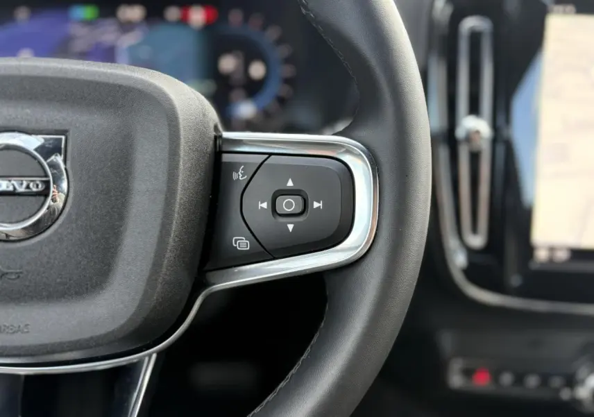Gros plan sur le côté droit du volant noir d'un Volvo XC40 2024 avec commandes intégrées et tableau de bord flou.