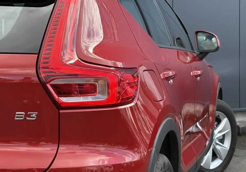 Vue arrière côté droit d'un Volvo XC40 B3 MHEV rouge fusion, mettant en valeur son feu arrière distinctif et ses jantes alliage.