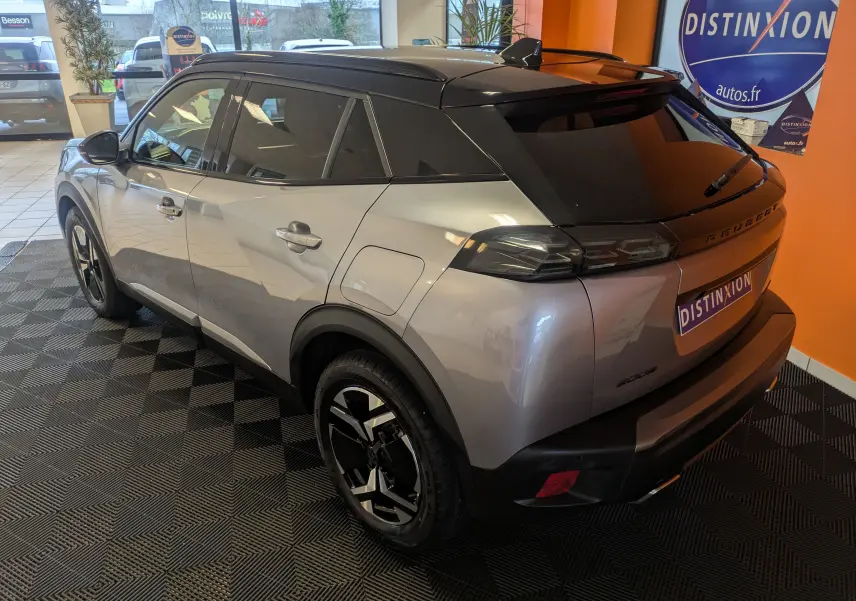 Vue 3/4 arrière droite du Peugeot 2008 Hybrid 145 e-DCS6 GT gris Artense avec toit noir et jantes bi-ton en showroom.