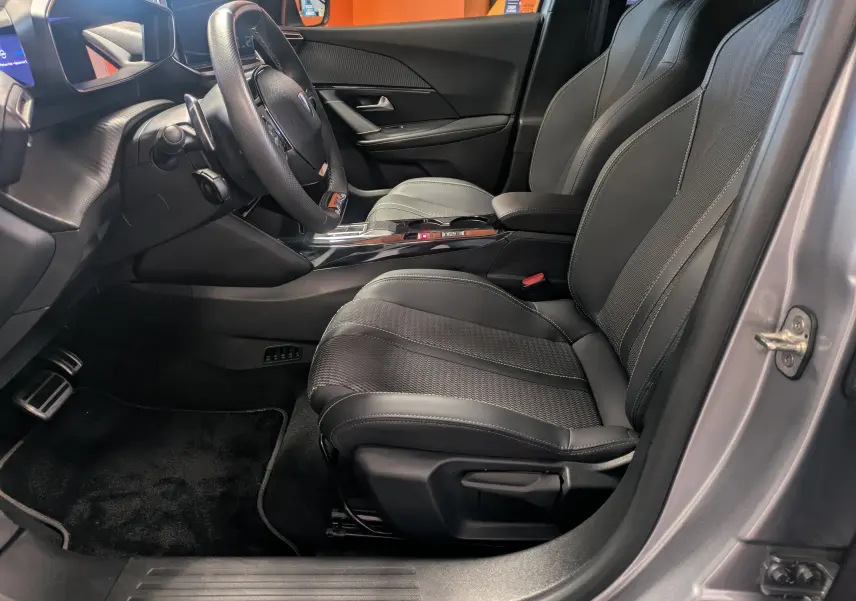 Vue intérieure côté conducteur de la Peugeot 2008 Hybrid 145 gris Artense, sièges en cuir noir avec surpiqûres contrastées.
