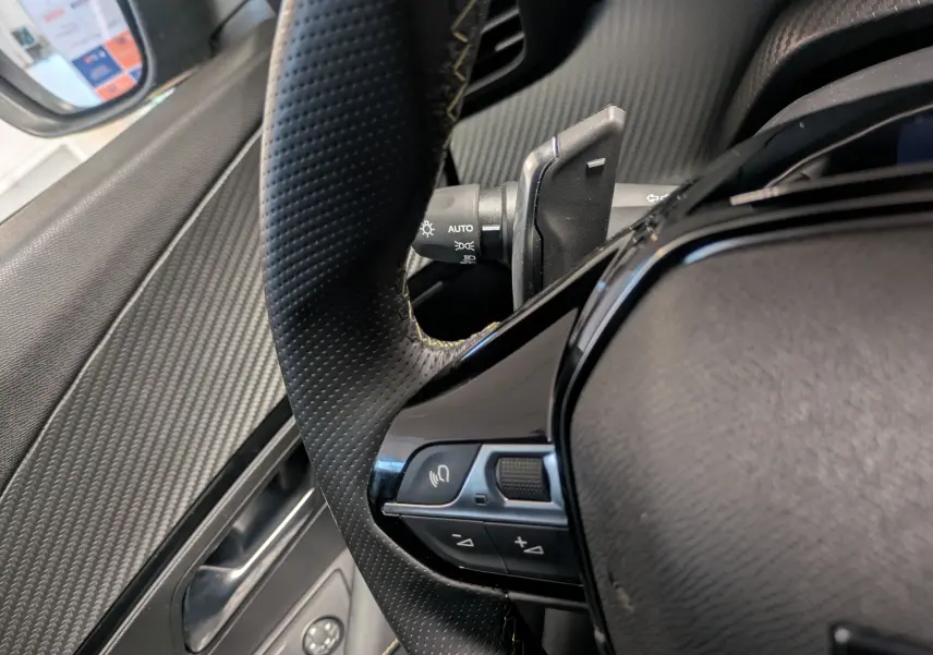 Gros plan sur le volant perforé et les commandes intégrées du Peugeot 2008 Hybrid 145 e-DCS6 GT, intérieur noir.