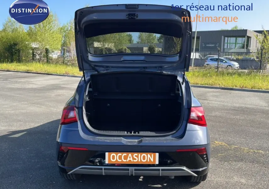 Vue arrière d'une Hyundai i20 gris aurora métal 2025 avec le coffre ouvert sur un parking extérieur.