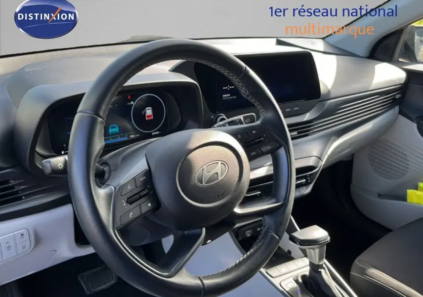 Vue intérieure du poste de conduite de la Hyundai i20 2025, volant cuir noir et tableau de bord gris aurora metal.