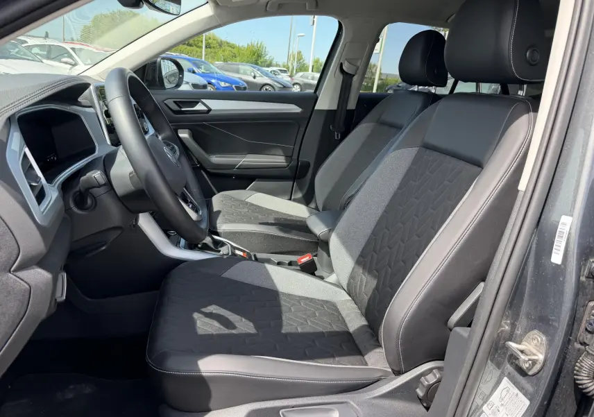 Vue intérieure côté conducteur du Volkswagen T-Roc gris 2025, mettant en valeur les sièges avant en tissu et cuir avec accoudoir central.