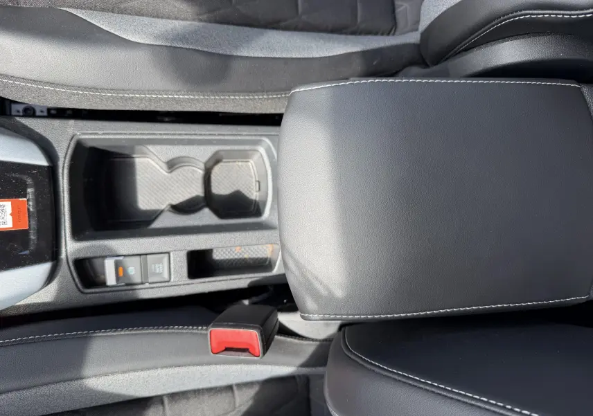 Vue plongeante sur la console centrale et accoudoir en cuir noir du Volkswagen T-Roc gris, avec porte-gobelets et frein électrique.