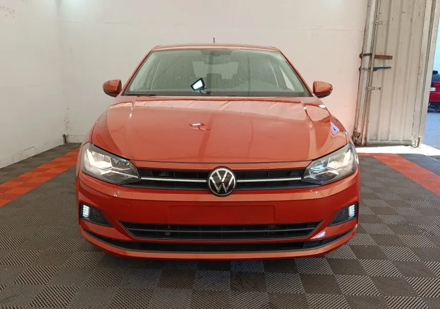 Vue de face d'une Volkswagen Polo 1.0 TSI 95 United orange avec phares et feux diurnes allumés dans un garage.