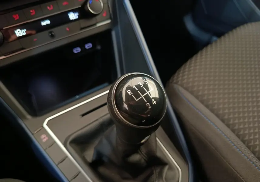 Gros plan sur le levier de vitesses manuel noir dans l’habitacle sombre de la Volkswagen Polo orange, siège tissu visible.