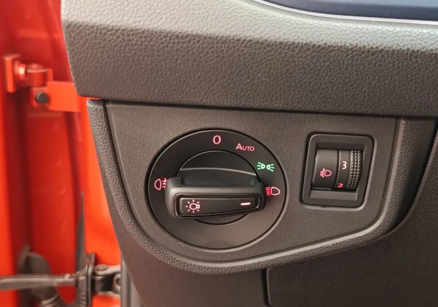 Gros plan sur le bouton de commande des phares dans l'habitacle d'une Volkswagen Polo orange, côté gauche.