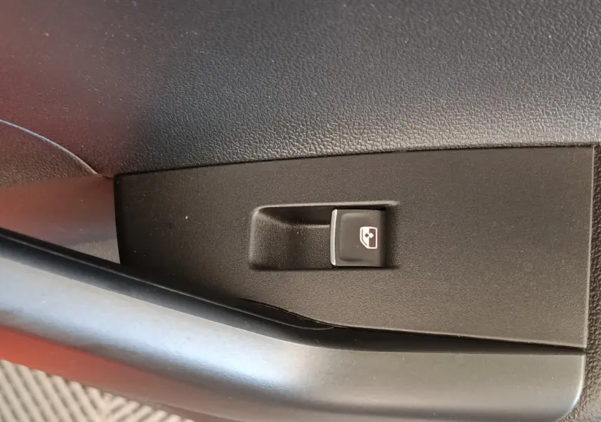 Gros plan sur le bouton de commande de la vitre électrique côté conducteur dans l'habitacle d'une Volkswagen Polo orange.