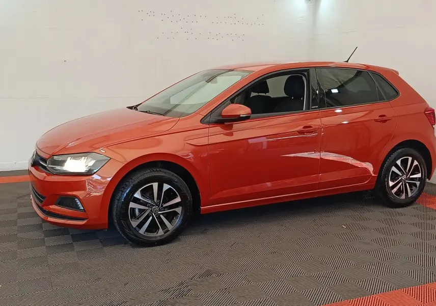 Vue de profil côté gauche d'une Volkswagen Polo orange 2020 avec jantes alliage et phares allumés.
