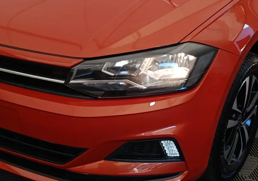 Gros plan sur l'avant droit orange vif du Volkswagen Polo 1.0 TSI 95 United avec phare LED et jante alliage noire.
