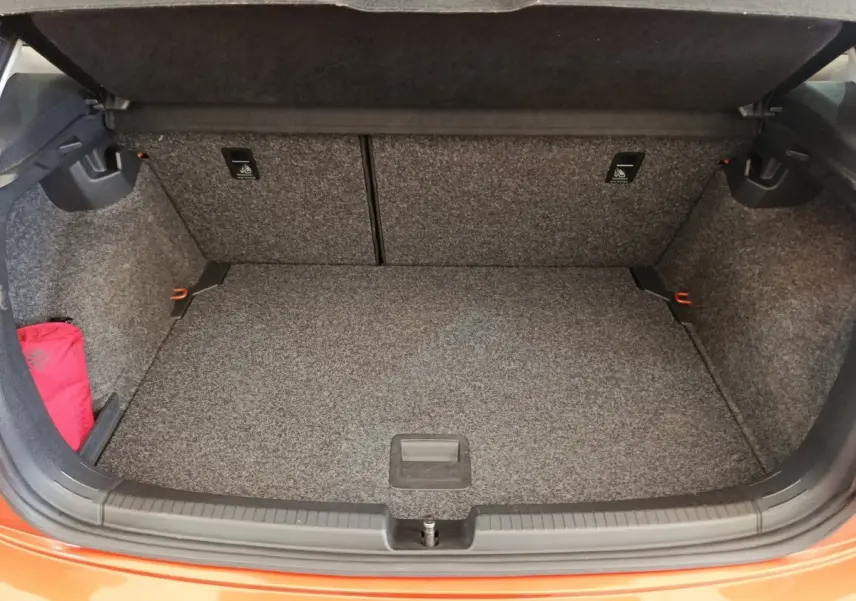 Coffre ouvert vu de face d'une Volkswagen Polo orange 2020, intérieur gris avec tapis de sol et rangement latéral.