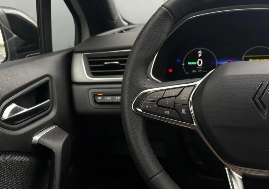 Gros plan sur le volant noir perforé et le tableau de bord numérique du Renault Captur hybride, côté conducteur.
