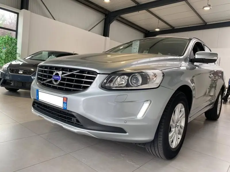 Vue 3/4 avant droite d'un Volvo XC60 argenté avec calandre chromée et phares halogènes en showroom.