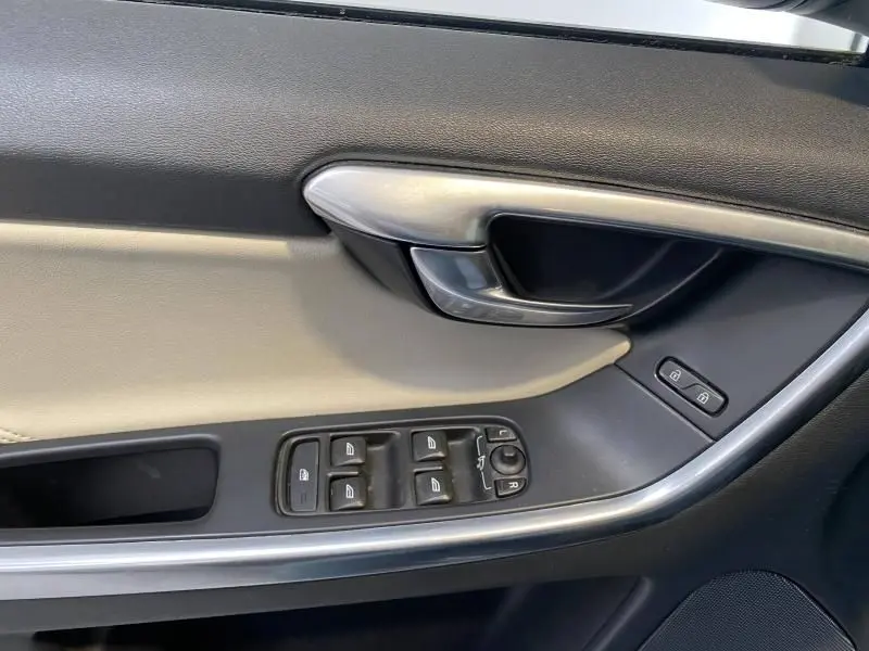 Gros plan sur la porte côté conducteur argentée et noire du Volvo XC60 2015 avec commandes électriques et poignée métal.