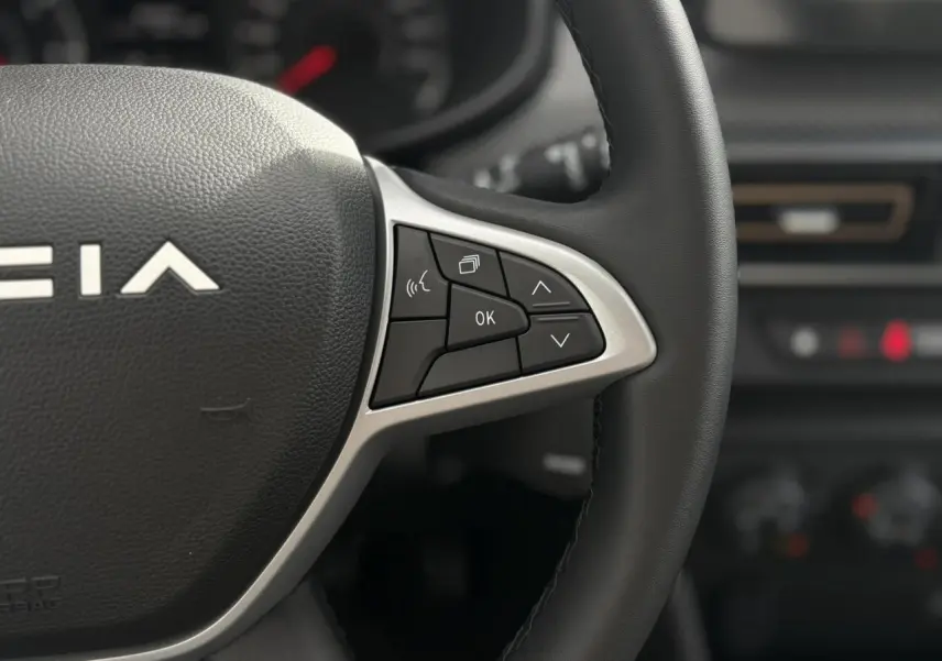 Gros plan sur les commandes du volant Soft Feel noir de la Dacia Sandero Stepway 2025, intérieur sombre flou en arrière-plan