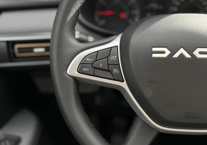 Gros plan sur le volant noir de la Dacia Sandero Stepway 2025 avec commandes de régulateur de vitesse intégrées.