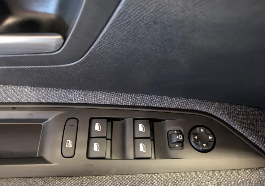 Vue rapprochée des commandes de lève-vitres et réglages des rétroviseurs sur la porte côté conducteur du Peugeot 3008 gris Arthense.