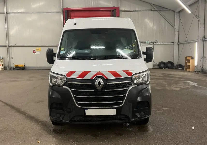 Vue avant d’un Renault Master cabine approfondie blanc avec marquage rouge et noir sur le pare-chocs dans un garage.