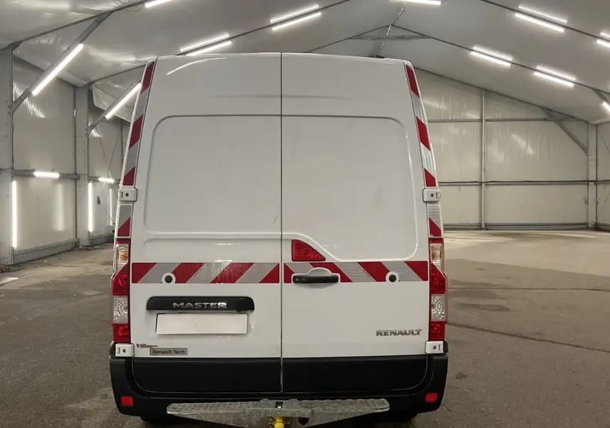 Vue arrière d’un Renault Master blanc avec bandes réfléchissantes rouges et blanches dans un grand hangar.