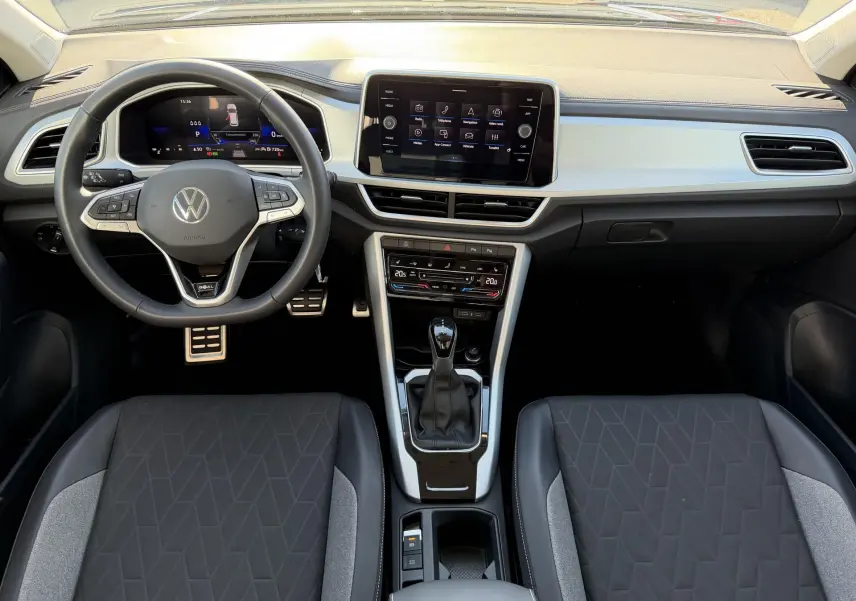 Vue intérieure frontale du tableau de bord et volant cuir noir du Volkswagen T-Roc 2025 avec écran tactile central et levier de vitesse.