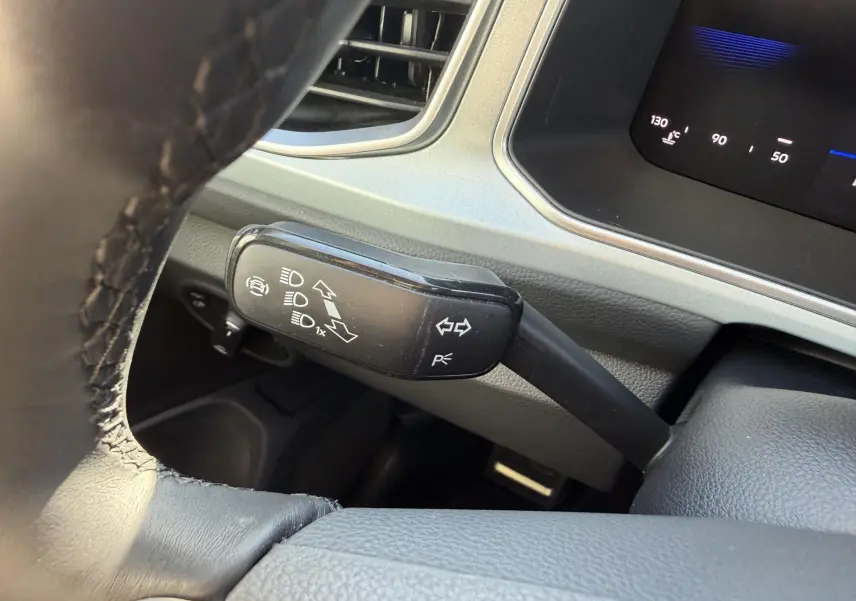 Gros plan sur la manette de clignotants noire à gauche du volant dans l’habitacle gris clair du Volkswagen T-Roc 2025.