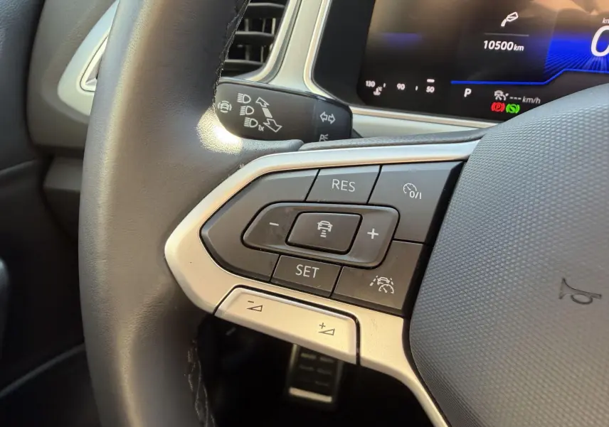 Gros plan sur le volant cuir multifonctions du Volkswagen T-Roc 2025, avec commandes du régulateur adaptatif visibles.