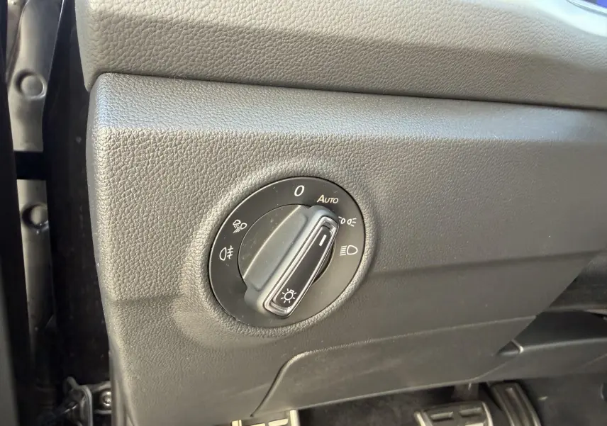 Gros plan sur le bouton de commande des phares dans l’habitacle noir du Volkswagen T-Roc 2025, côté conducteur.