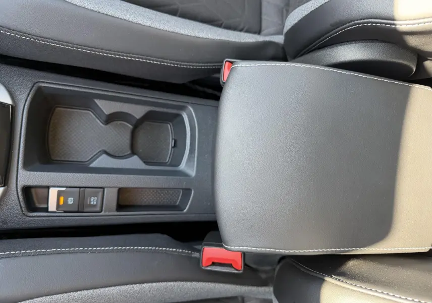 Vue rapprochée de la console centrale noire du Volkswagen T-Roc 2025, avec accoudoir et porte-gobelets.