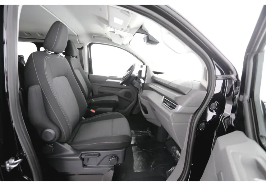 Vue intérieure côté conducteur du Volkswagen Transporter T7 ProCab 2025, sièges tissu gris et tableau de bord moderne.