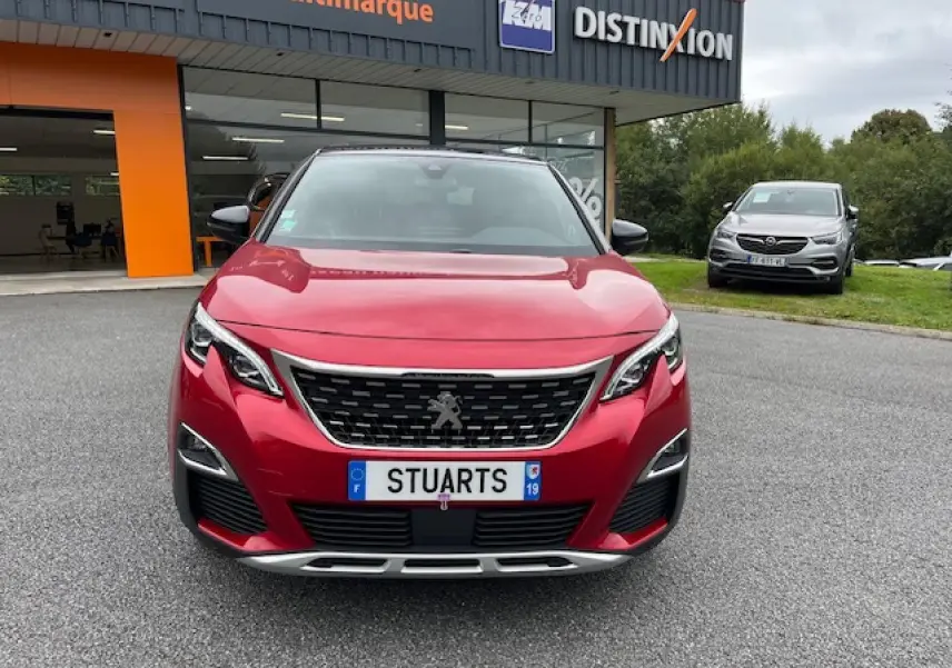 Vue frontale d'un Peugeot 3008 GT Line rouge Ultimate avec calandre chromée et projecteurs LED, devant un showroom.