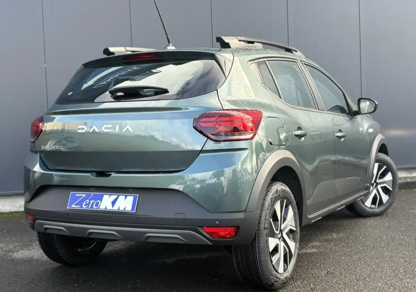 Vue 3/4 arrière droite d'une Dacia Sandero Stepway 2025 vert cèdre avec barres de toit et jantes spécifiques.