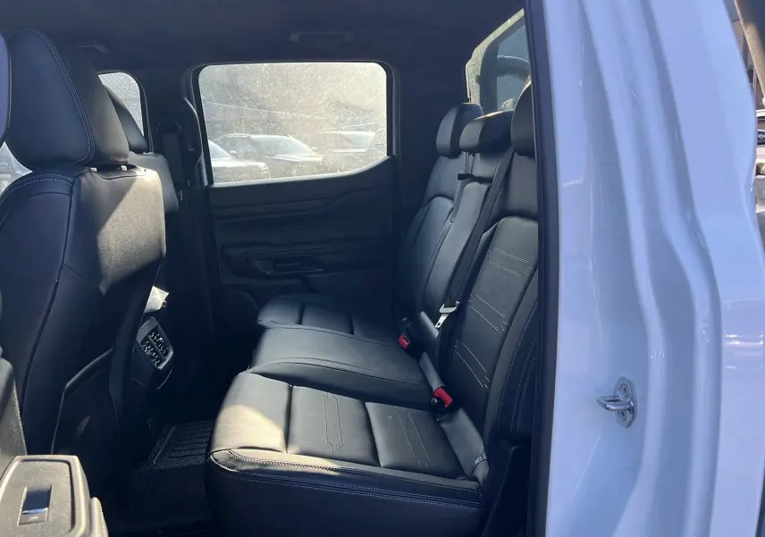 Intérieur arrière du Ford Ranger 2025 blanc glacier, vue côté gauche montrant les sièges en cuir noir et les ceintures de sécurité.