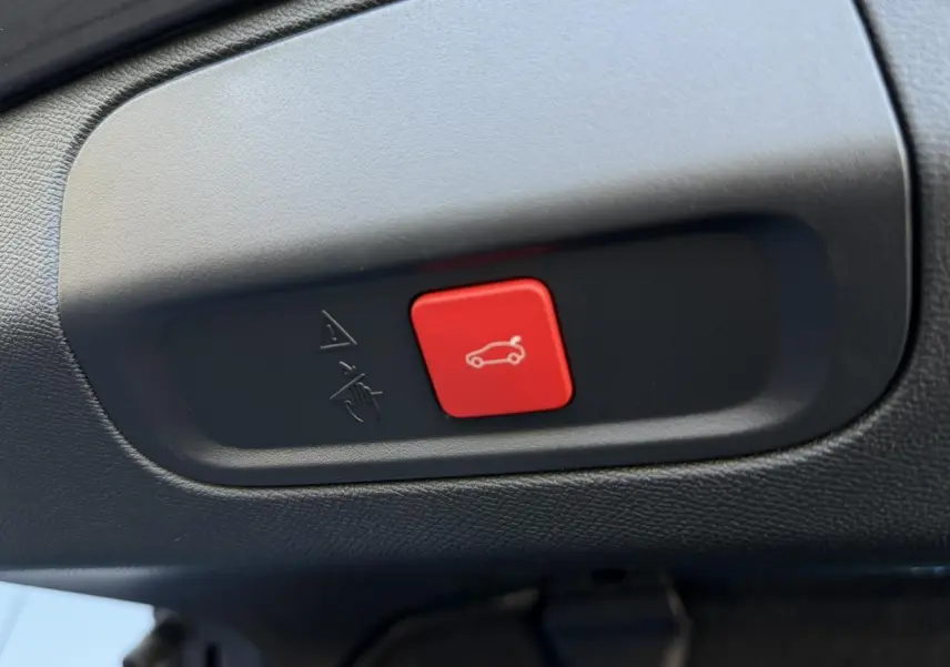 Gros plan sur le bouton rouge d'ouverture du hayon dans l'habitacle noir du Peugeot 408 Hybrid blanc Okenite.