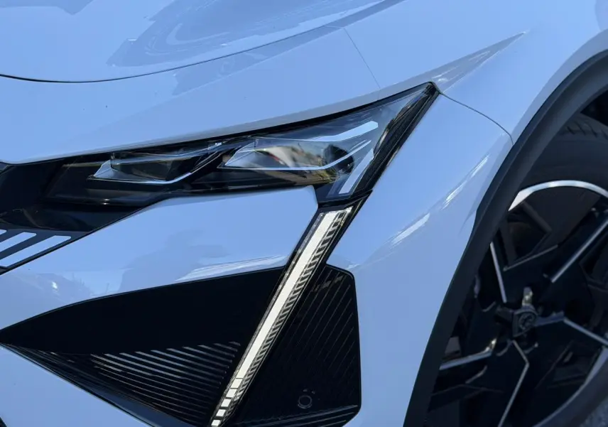 Gros plan sur le phare avant droit blanc Okenite du Peugeot 408 Hybrid 145 e-DSC6 GT avec jante alliage noire diamantée.