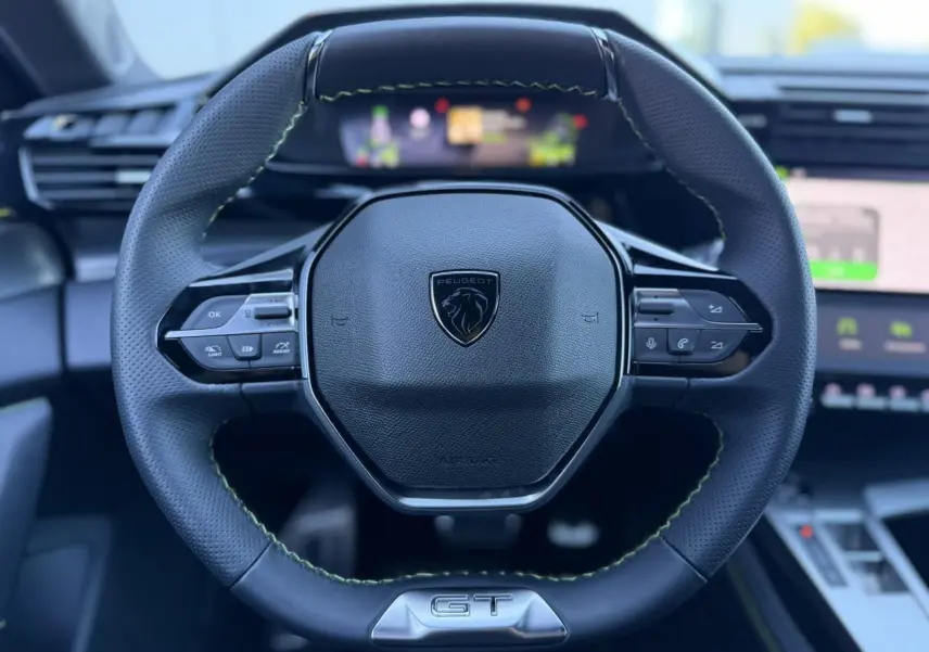 Gros plan sur le volant cuir perforé noir avec surpiqûres vertes et logo GT du Peugeot 408 Hybrid 2025.