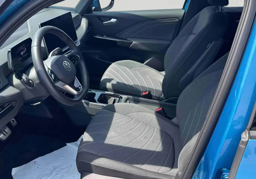 Vue intérieure côté conducteur du Volkswagen ID.3 bleu, montrant sièges gris et tableau de bord digital.