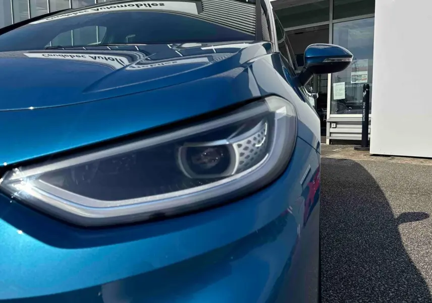 Gros plan sur le phare avant droit d’une Volkswagen ID.3 2025 bleu métallisé avec rétroviseur assorti.