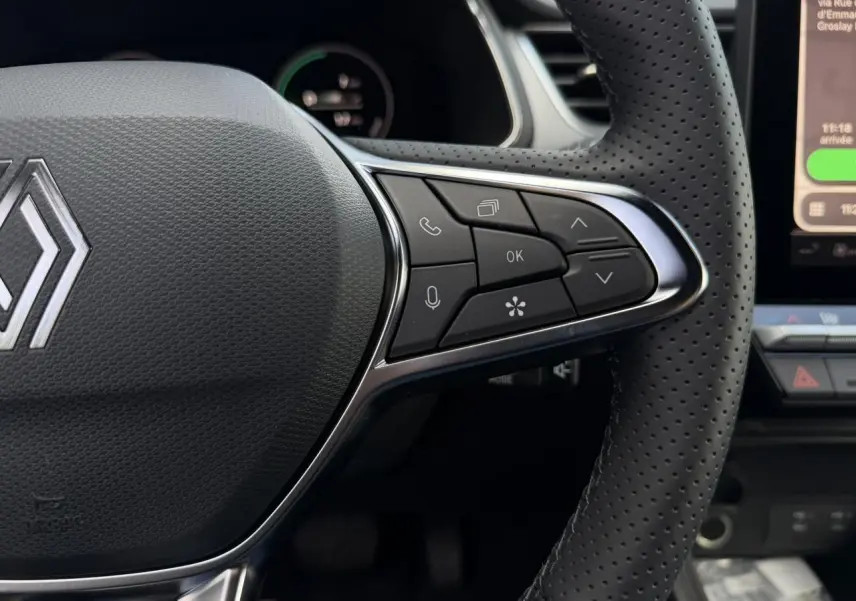 Gros plan sur le volant en cuir perforé noir du Renault Captur 2026 avec commandes multifonctions et logo central chromé.