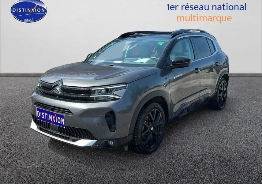 Citroën C5 Aircross gris platinium en 3/4 avant droit, avec jantes noires et barres de toit visibles.