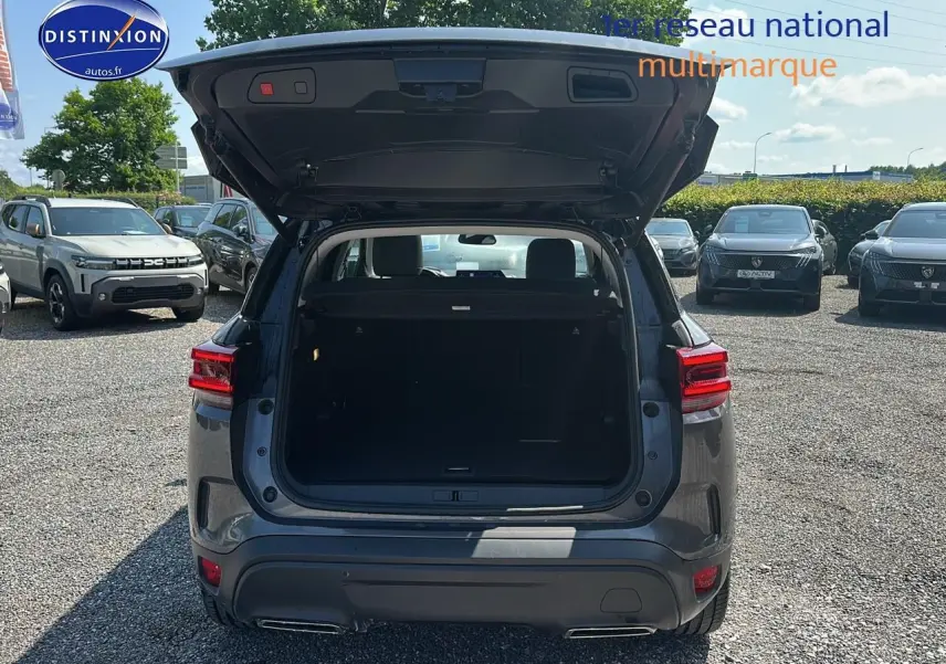 Vue arrière d'un Citroën C5 Aircross gris platinium 2024 avec hayon ouvert et coffre visible sur parking.