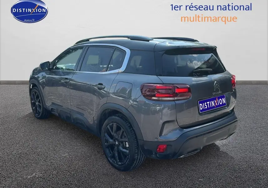 Vue 3/4 arrière droite d'un Citroën C5 Aircross gris platinium avec jantes noires et barres de toit.