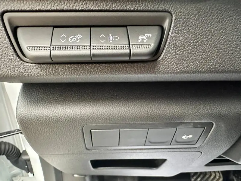 Boutons de réglage d'éclairage et de contrôle de stabilité sur la planche de bord inférieure d'un Nissan Townstar blanc 2024.